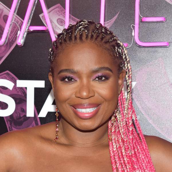 A Black woman, Katori Hall, is seen from the chest up, smiling, in a pink, heart-shaped boostier, and long pink and blonde cornrows