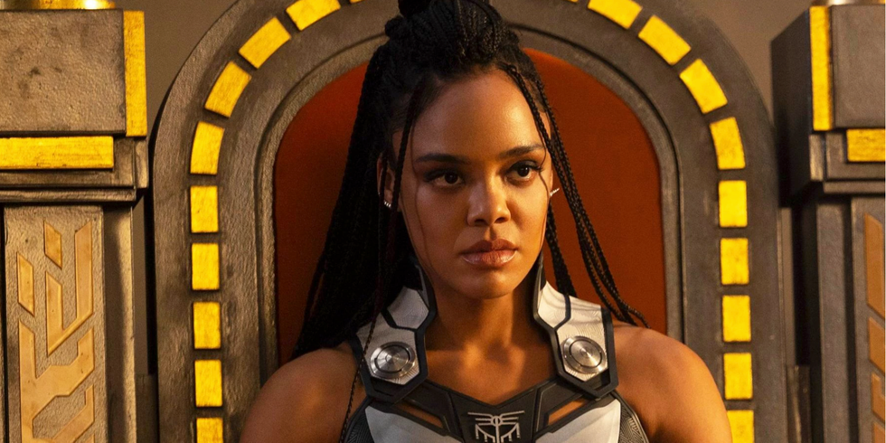 A Black woman, Tessa Thompson, sits on a throne, wearing box braids, with a serious look on her face