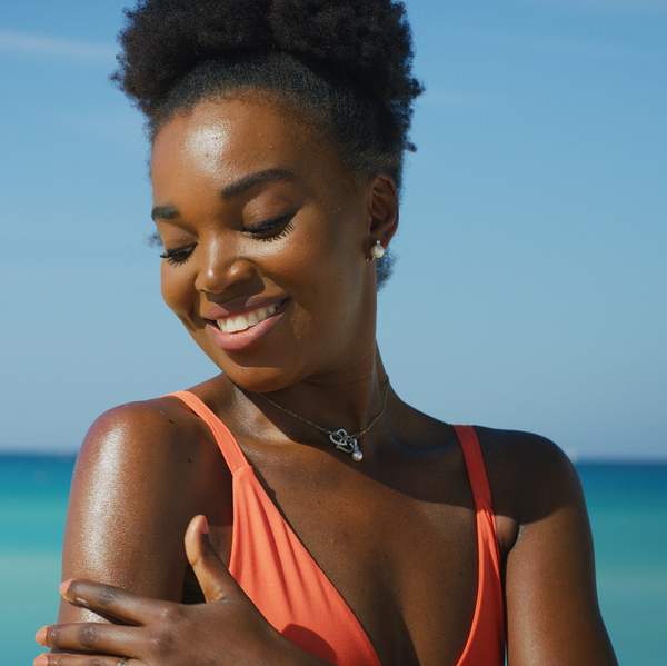A happy young african woman is applying a sunscreen or sun tanning lotion to take care of her skin during a vacation on a beach.
