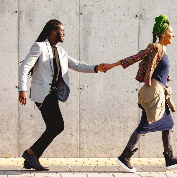 A-young-woman-runs-across-the-sidewalk-and-laughs-leading-the-young-man-by-the-hand