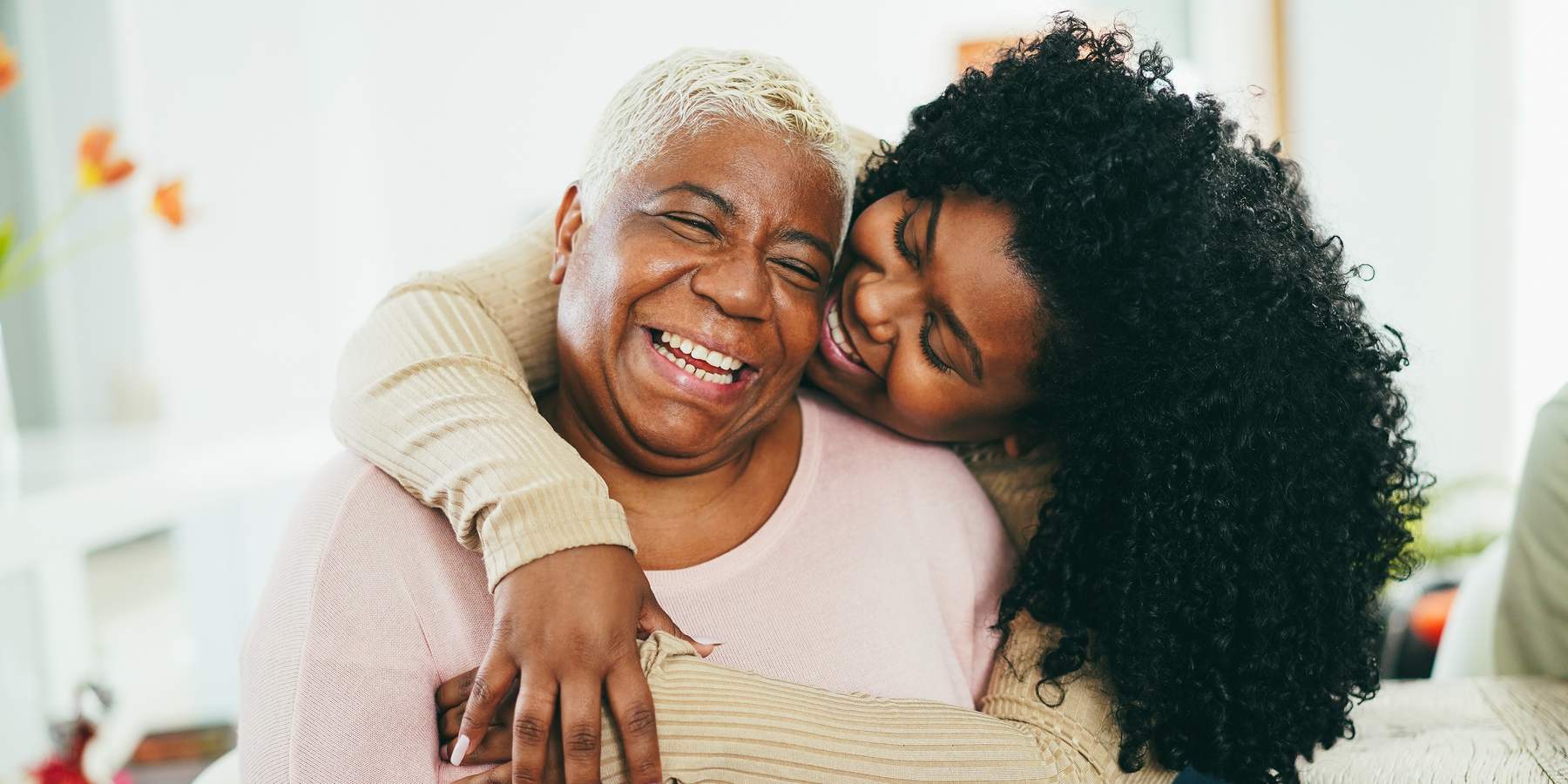 African daughter hugging her mum indoors at home - Main focus on senior mother face