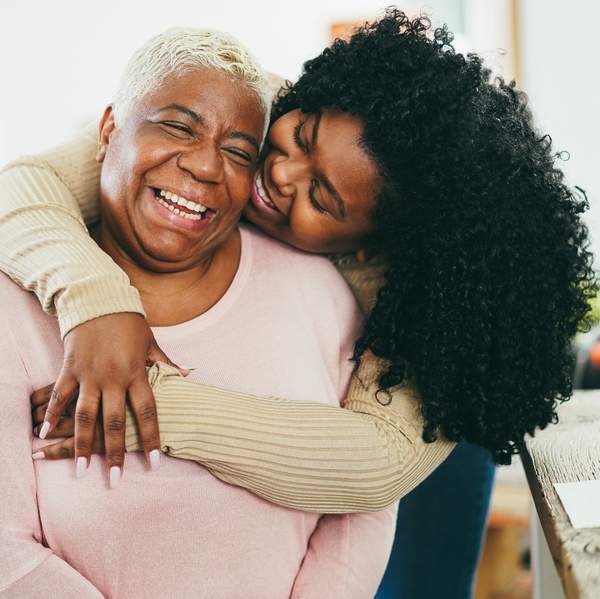 African daughter hugging her mum indoors at home - Main focus on senior mother face