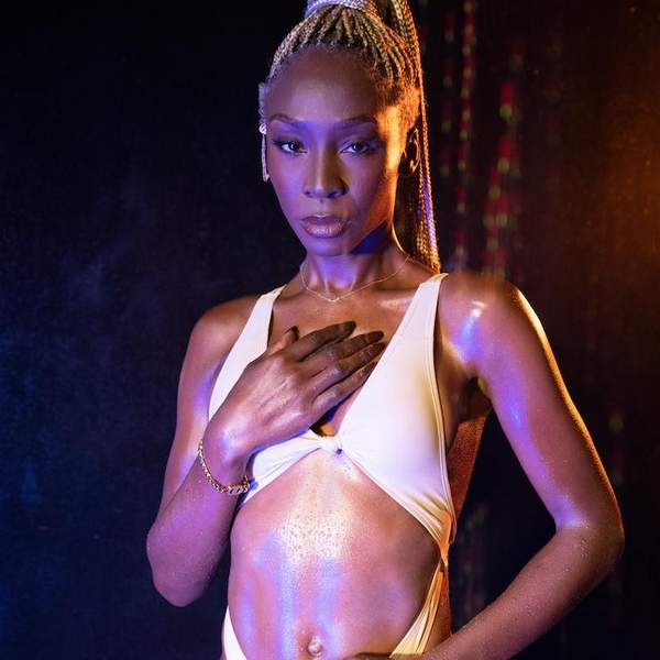 Angelica Ross, Black woman stands looking at the camera wearing a low-cut, cut-out dress, exposing her stomach. Her hand is over her heart