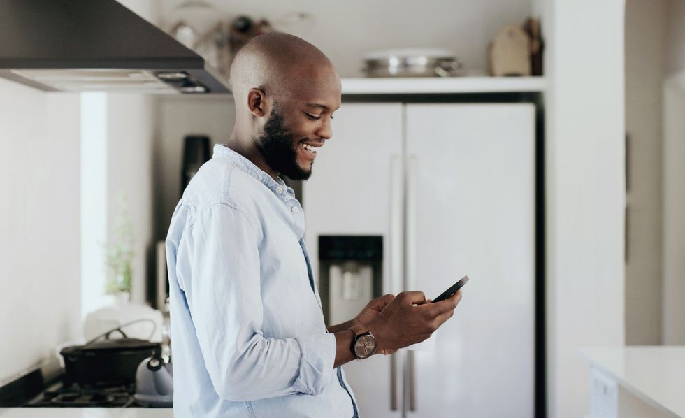 Bald-Black-man-smiling-as-he-checks-his-phone-in-the-kitchen