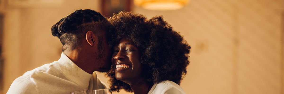 Beautiful passionate african american couple having a romantic candlelight dinner at home and celebrating their love together. Concept of love and relationship. Kissing and bonding. Copy space.
