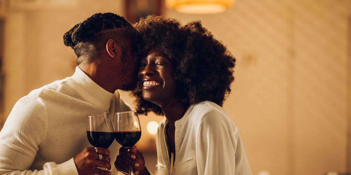 Beautiful passionate african american couple having a romantic candlelight dinner at home and celebrating their love together. Concept of love and relationship. Kissing and bonding. Copy space.