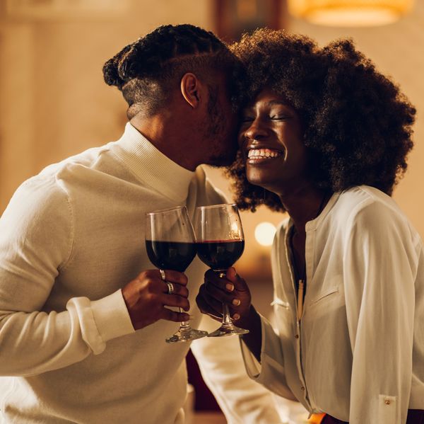 Beautiful passionate african american couple having a romantic candlelight dinner at home and celebrating their love together. Concept of love and relationship. Kissing and bonding. Copy space.