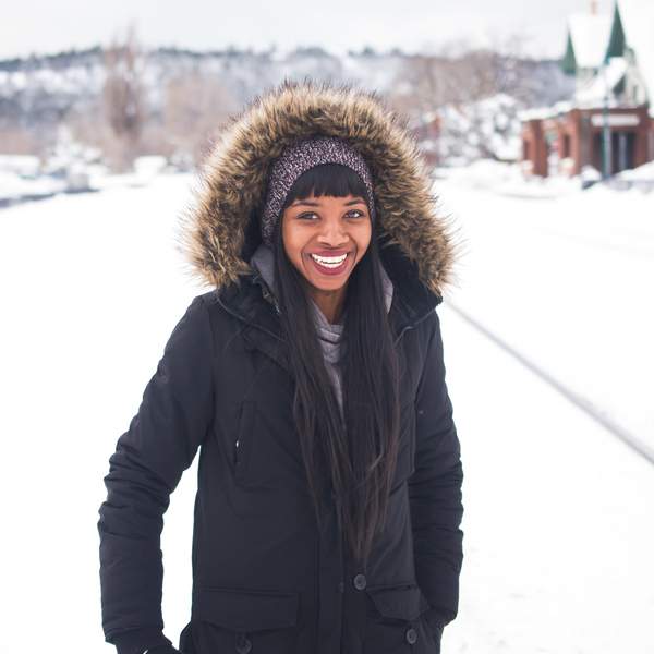 Black-woman-wearing-coat-standing-on-snow-and-smiling-during-daytime