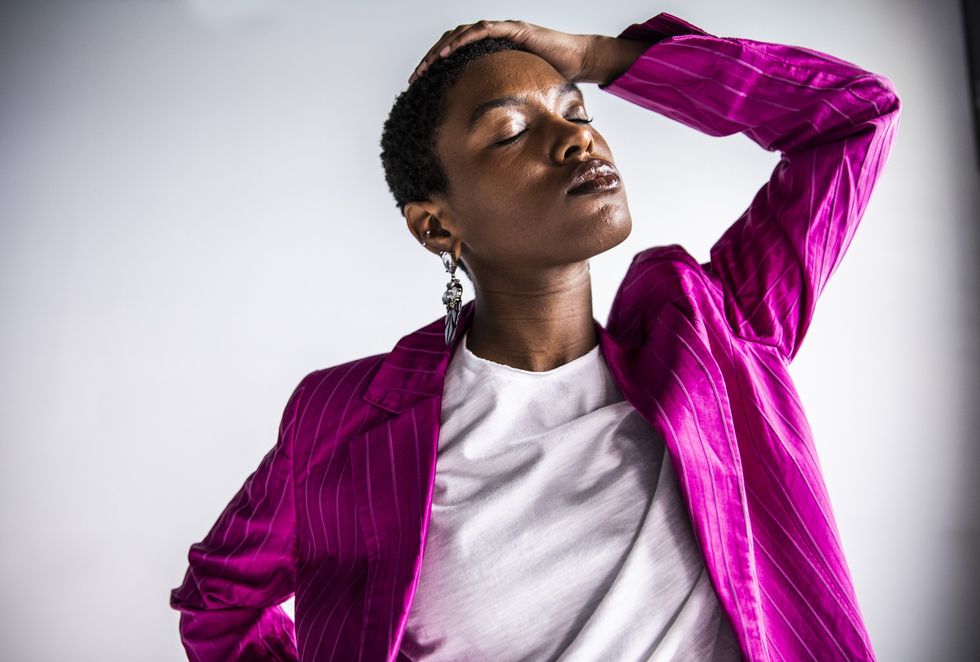 Black-woman-with-eyes-closed-holding-her-head-wearing-bright-fuschia-blazer