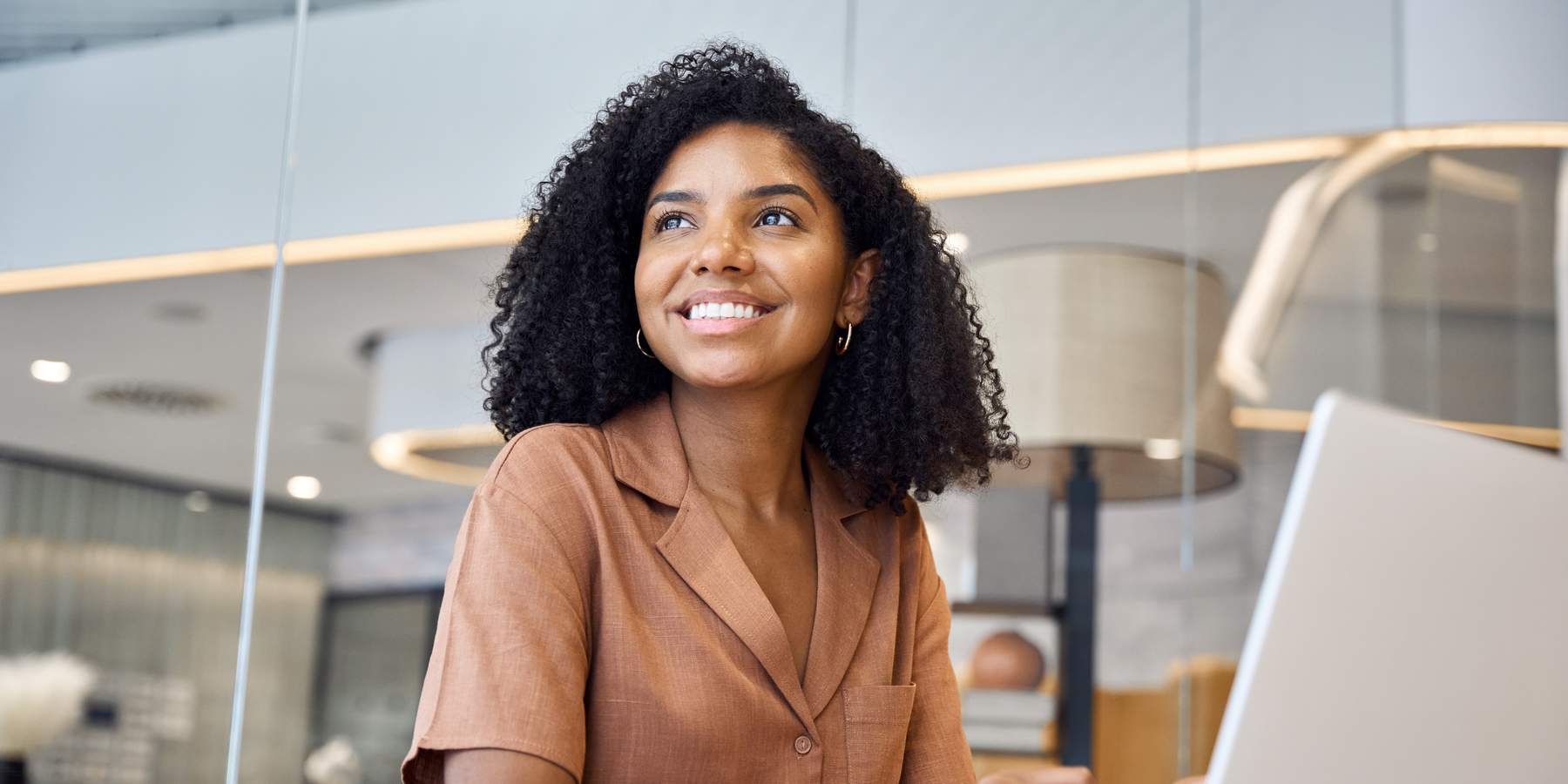 Busy happy young African American business woman employee using laptop at work in modern office. Professional businesswoman executive, company worker or manager looking away working at computer.