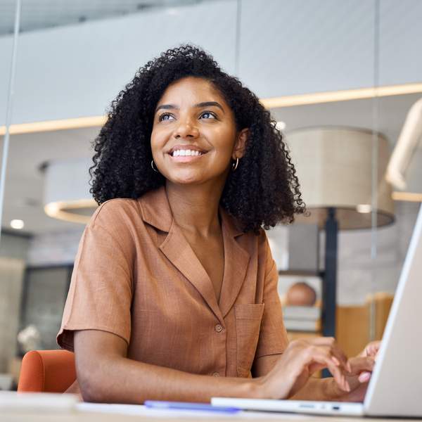Busy happy young African American business woman employee using laptop at work in modern office. Professional businesswoman executive, company worker or manager looking away working at computer.