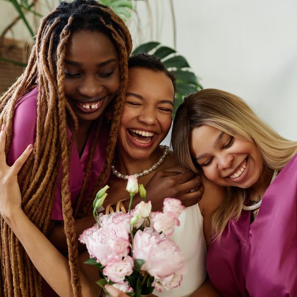Candid waist up portrait of happy black woman as young bride embracing bridesmaids during wedding ceremony