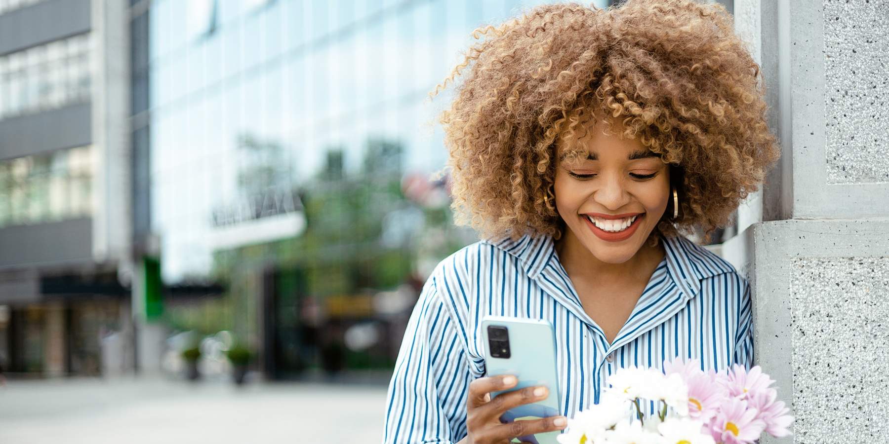 cheerful-woman-smiling-on-the-street-while-on-a-call-holding-flowers