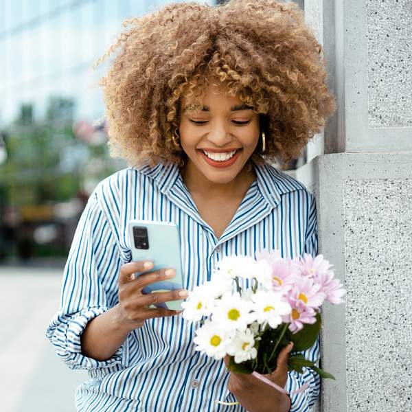 cheerful-woman-smiling-on-the-street-while-on-a-call-holding-flowers