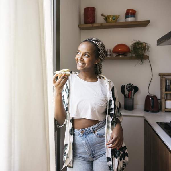 Cheerful-young-woman-eating-avocado-toast-breakfast-at-home