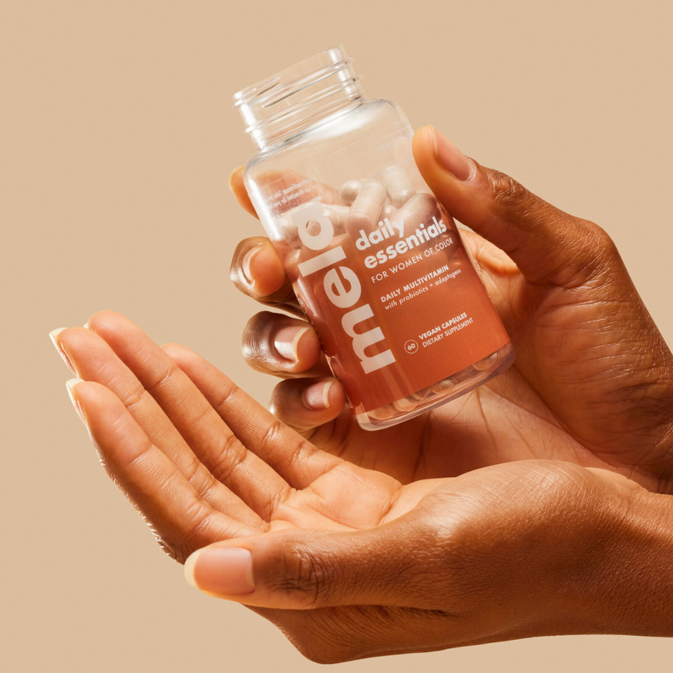 close-up-of-hands-with-open-palm-facing-upward-and-other-hand-holding-open-bottle-of-Mela-Vitamins