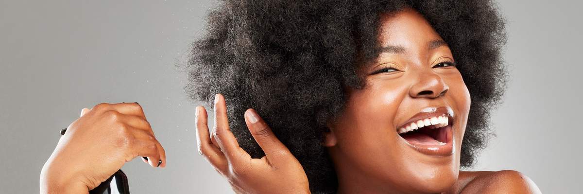Happy-Black-woman-spraying-her-afro-with-bond-building-treatment