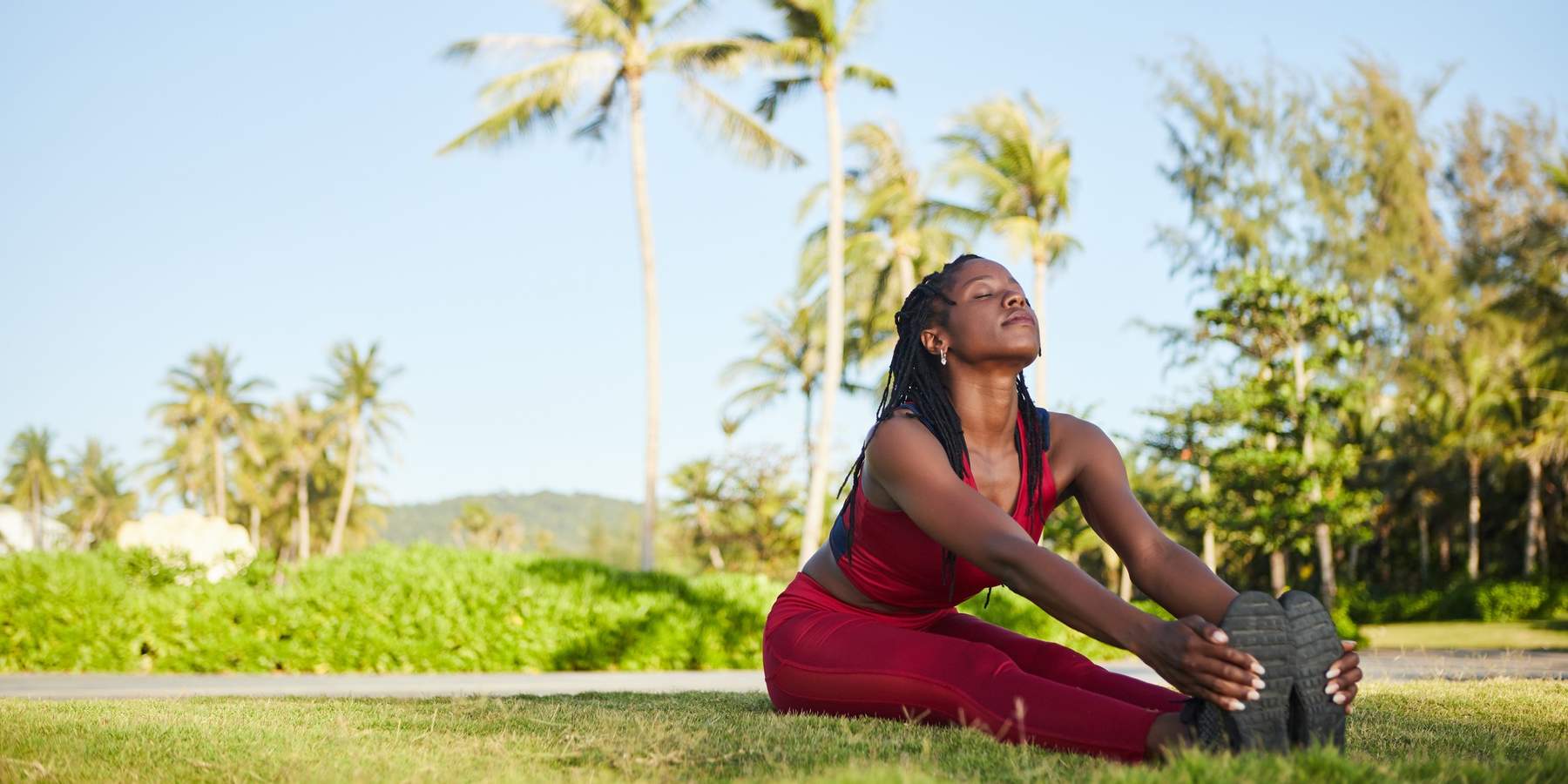 Happy-woman-sitting-on-ground-legs-straight-and-together-holding-her-feet-in-a-stretch