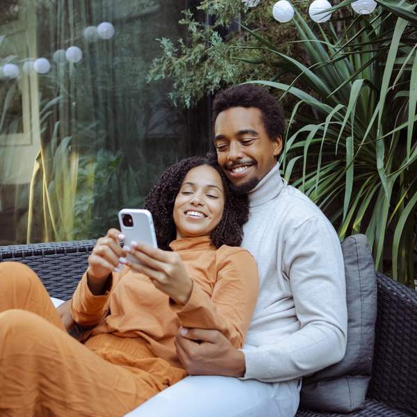 Happy-young-African-American-couple-enjoying-leisure-time-together-while-scrolling-phone-dating-apps