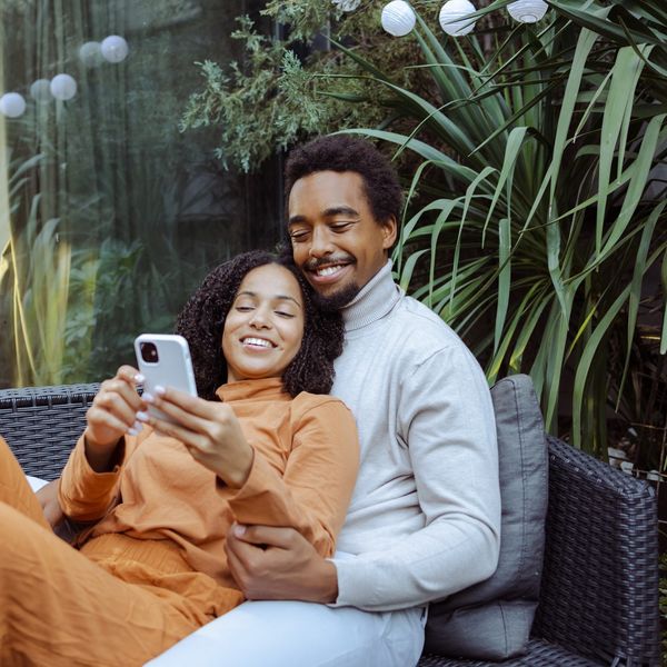 Happy-young-African-American-couple-enjoying-leisure-time-together-while-scrolling-phone-dating-apps