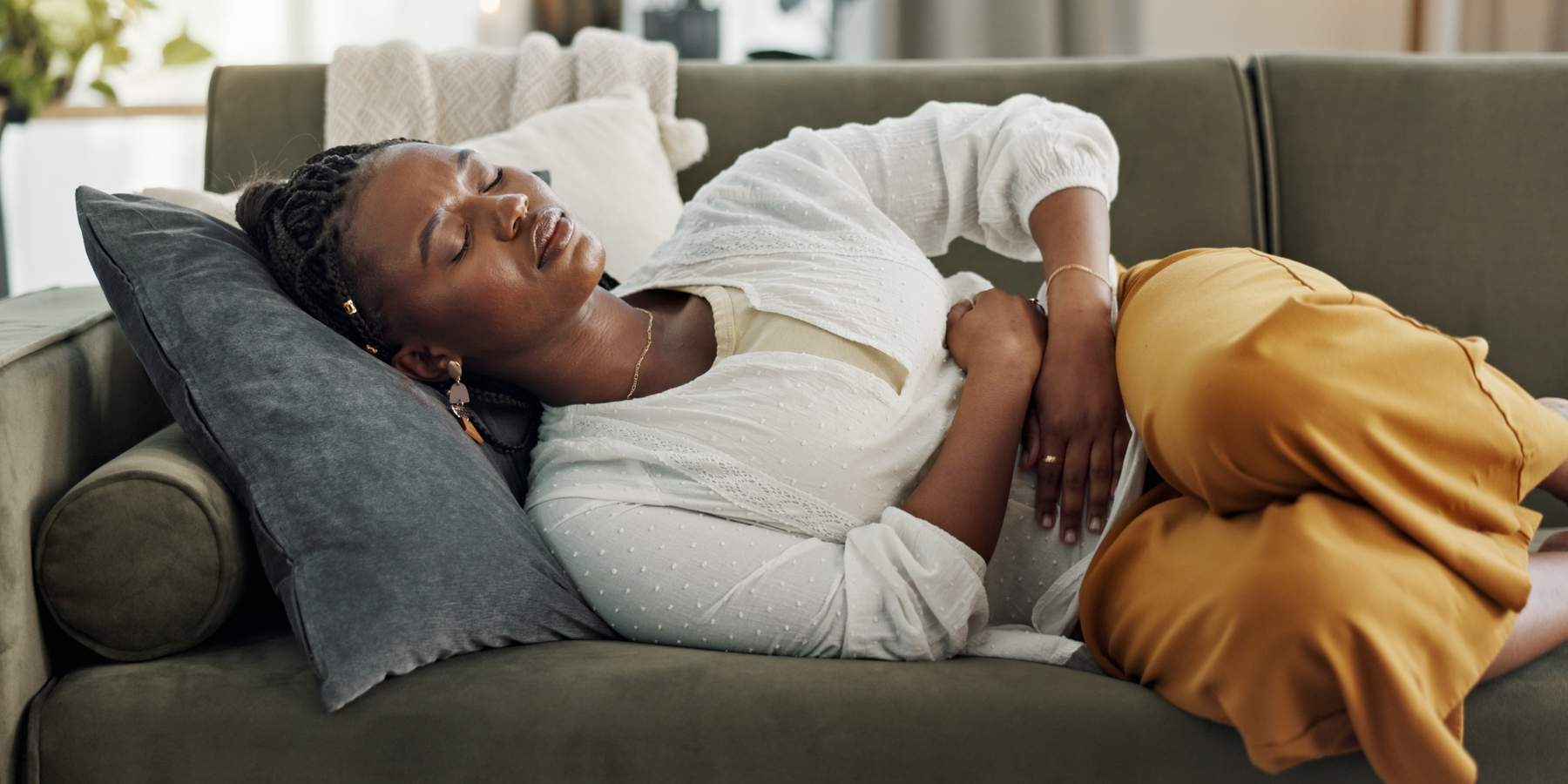 Home, pain and black woman on a couch, cramps and stomach with sickness, suffering and disease in the living room. African person, apartment and girl with abdominal problem, tummy ache and period