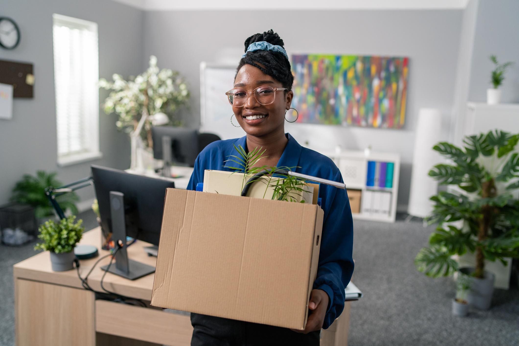 Black woman smiling with box of things from her office space