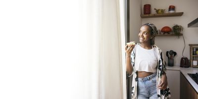 Cheerful-young-woman-eating-avocado-toast-breakfast-at-home