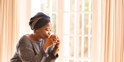 Young-woman-sitting-in-bedroom-drinking-hot-beverage-in-peace