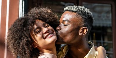 Young-man-kissing-girlfriend-on-the-cheek-outdoors