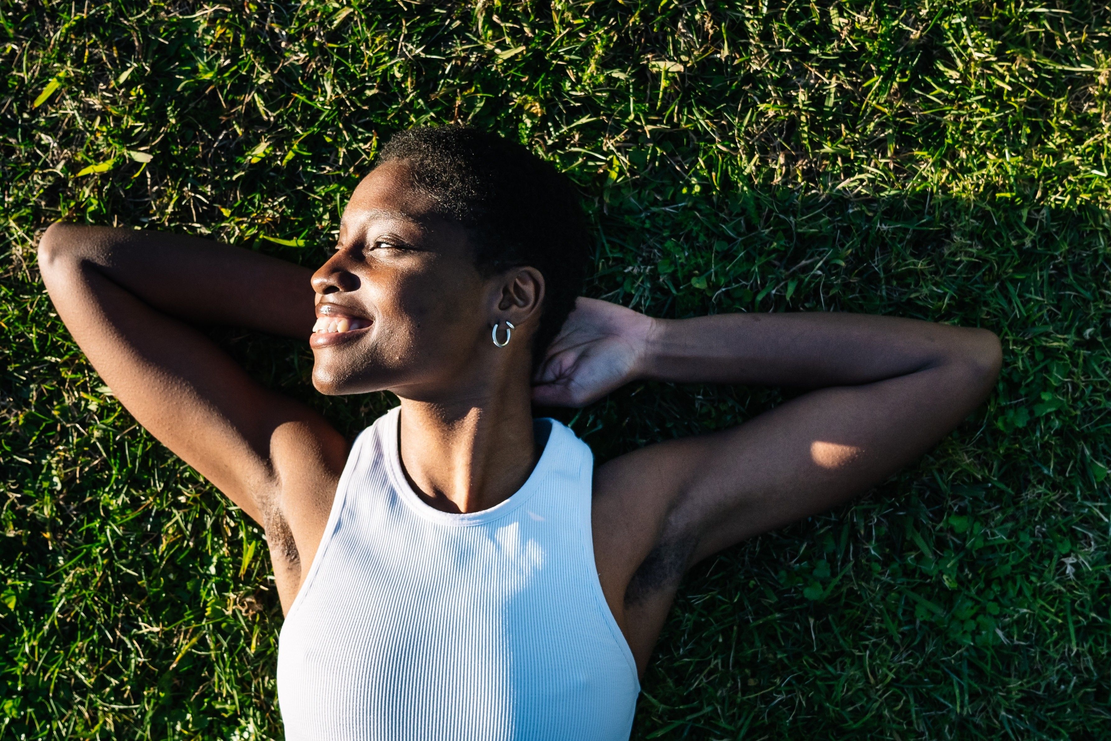 Young black woman relaxing lying on green grass smiling with hands behind head