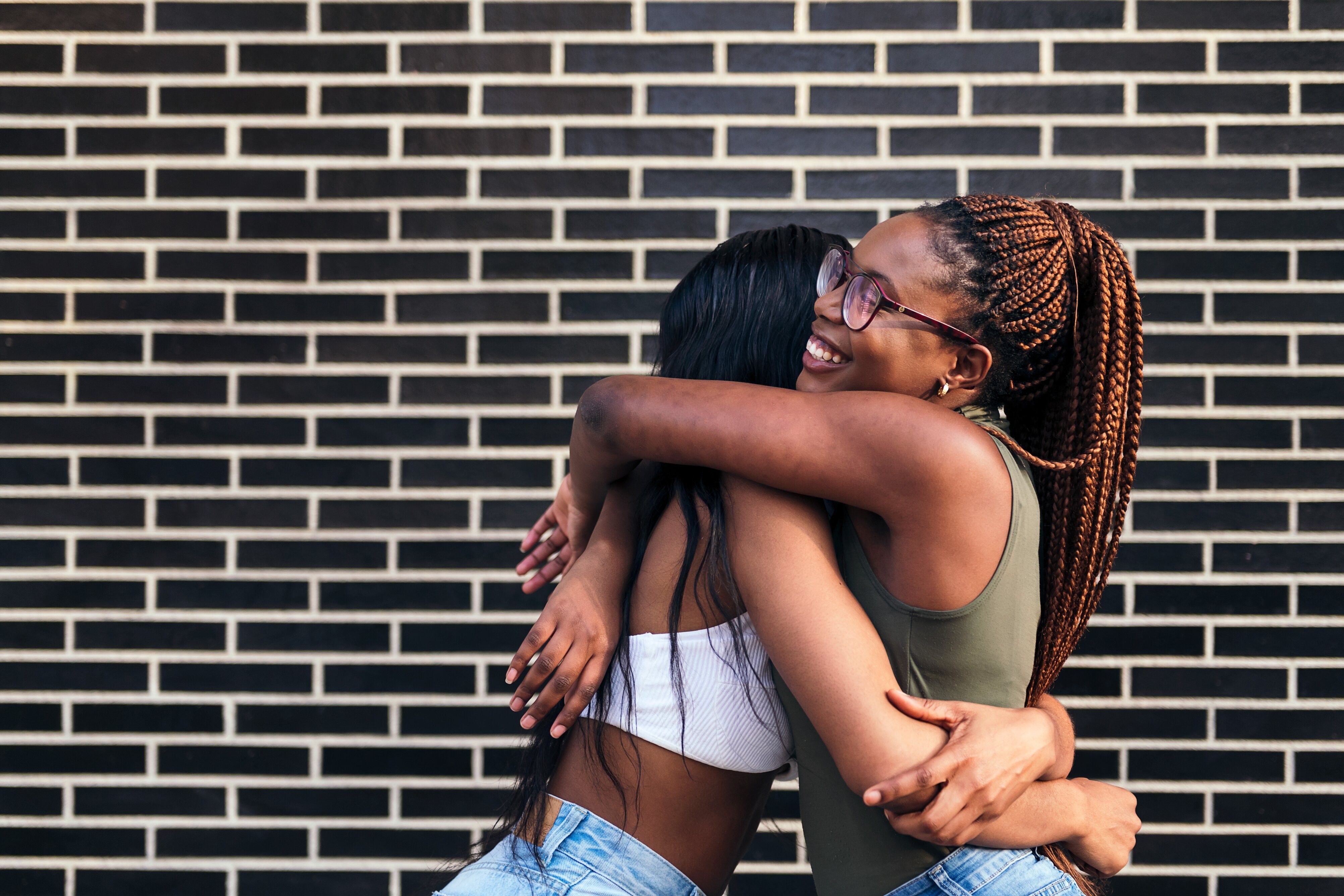young african women smiling happy and hugging each other in front of a brick wall, concept of youth and friendship, copy space for text