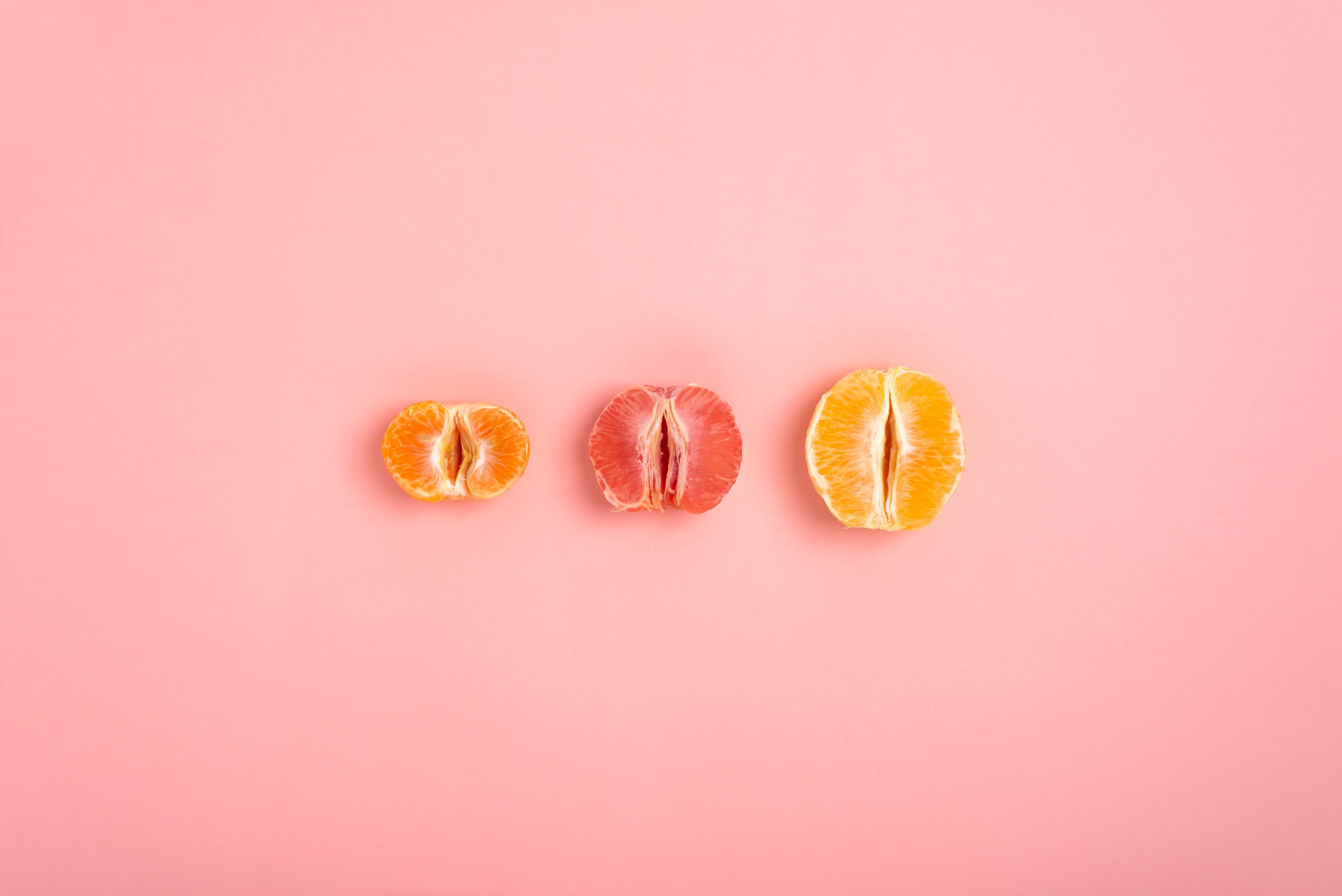 tangerine, grapefruit and orange cut in half on a peach background as a symbol of the vagina and female fertility, no people