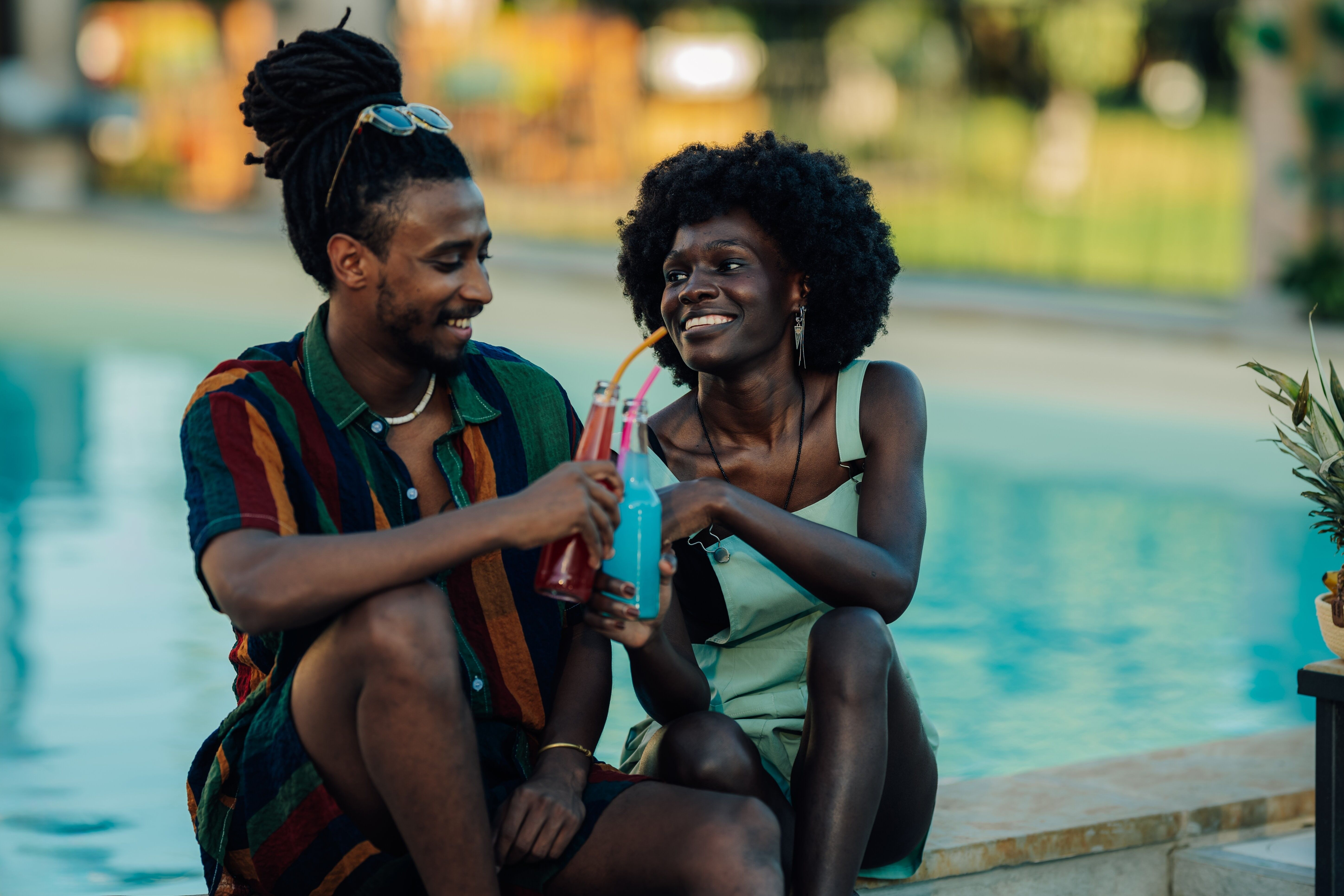Young couple toasting with colorful beverages, enjoying a relaxing moment by the pool during summer vacation, celebrating their love and togetherness in a vibrant and refreshing setting