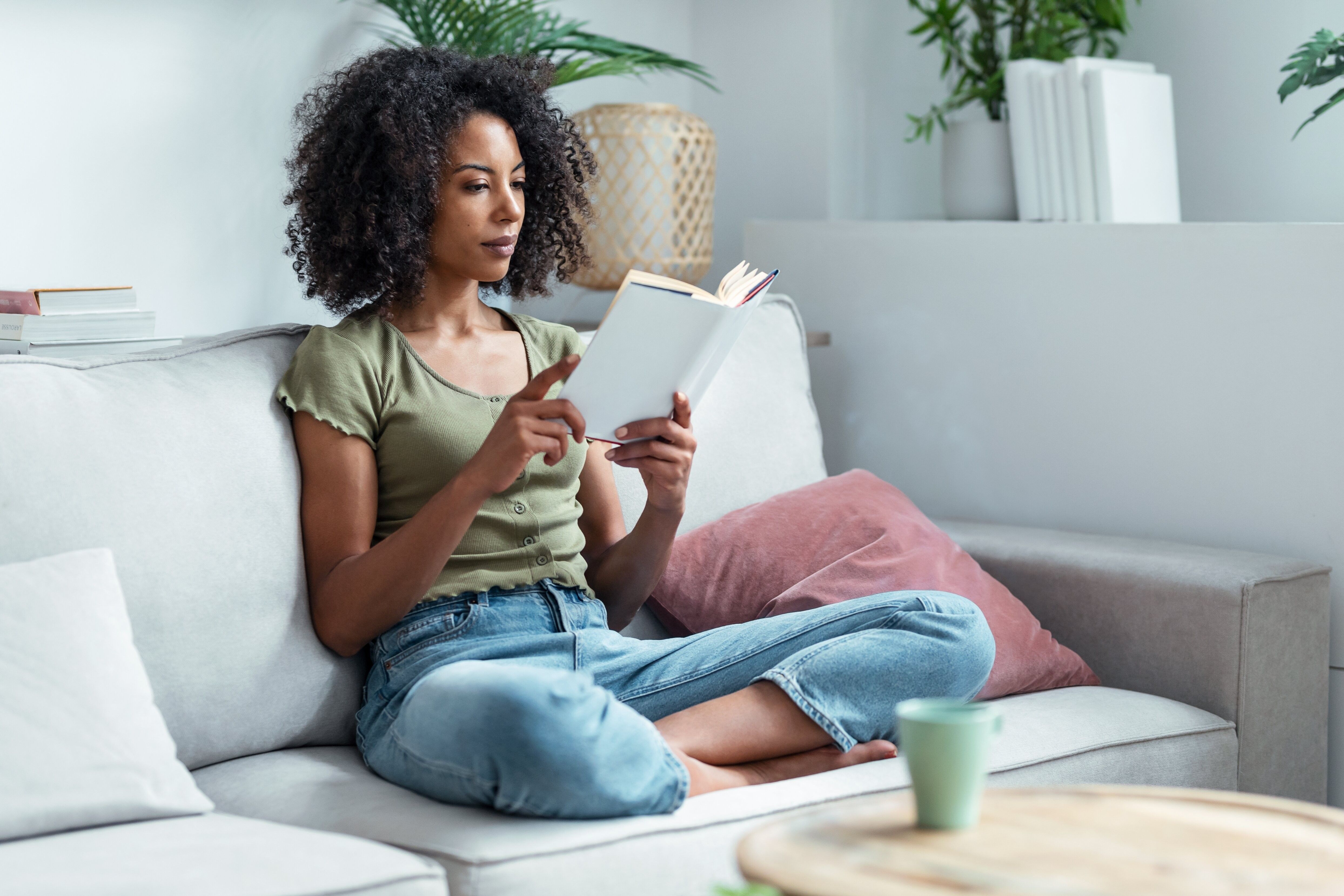 Shot of pretty young woman reading a book while sitting on sofa at home.