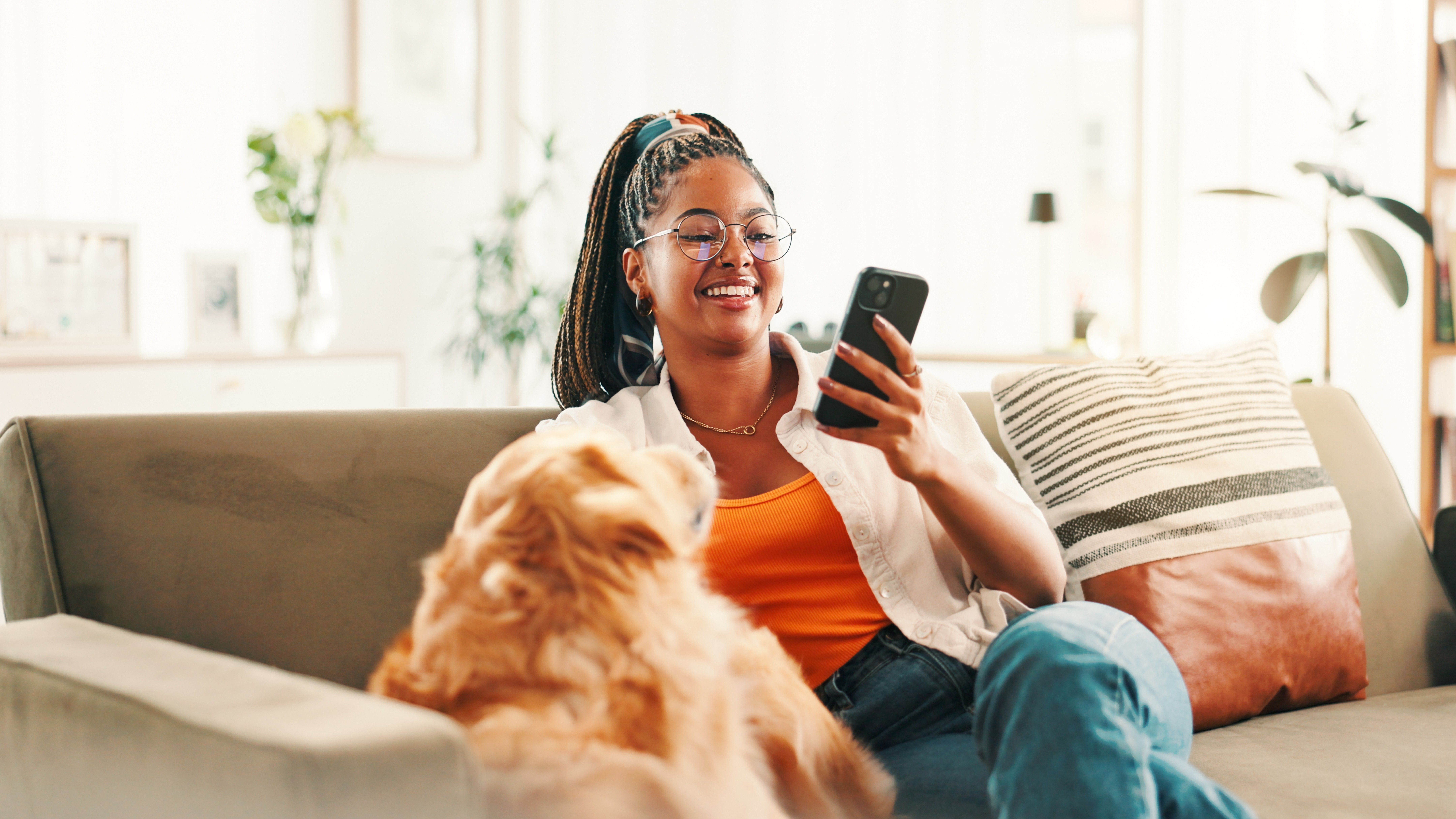 Black woman relaxing on sofa with dog while scrolling on smartphone
