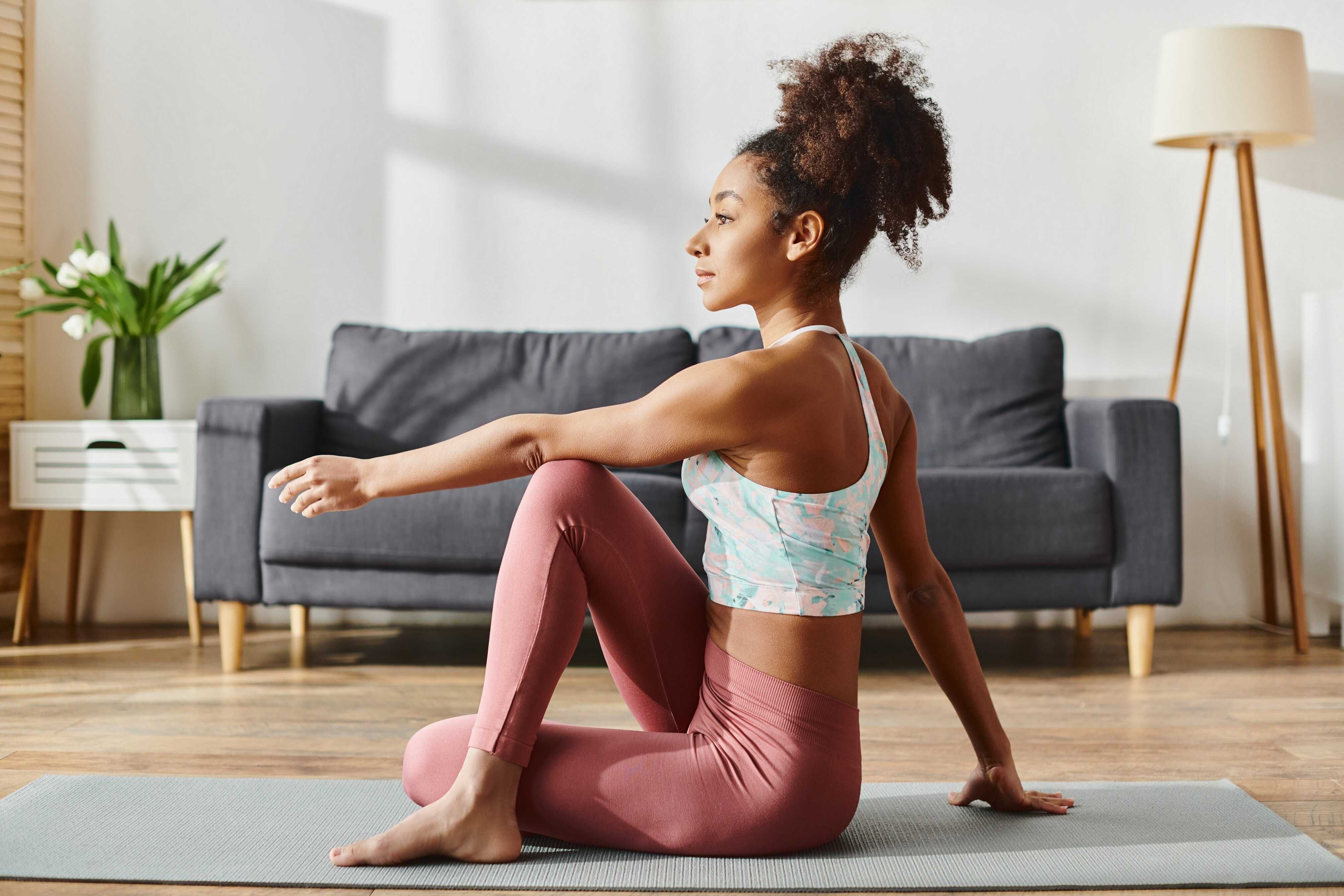 Curly Black woman in activewear gracefully doing Ayurveda-inspired fall practice of yoga at home.