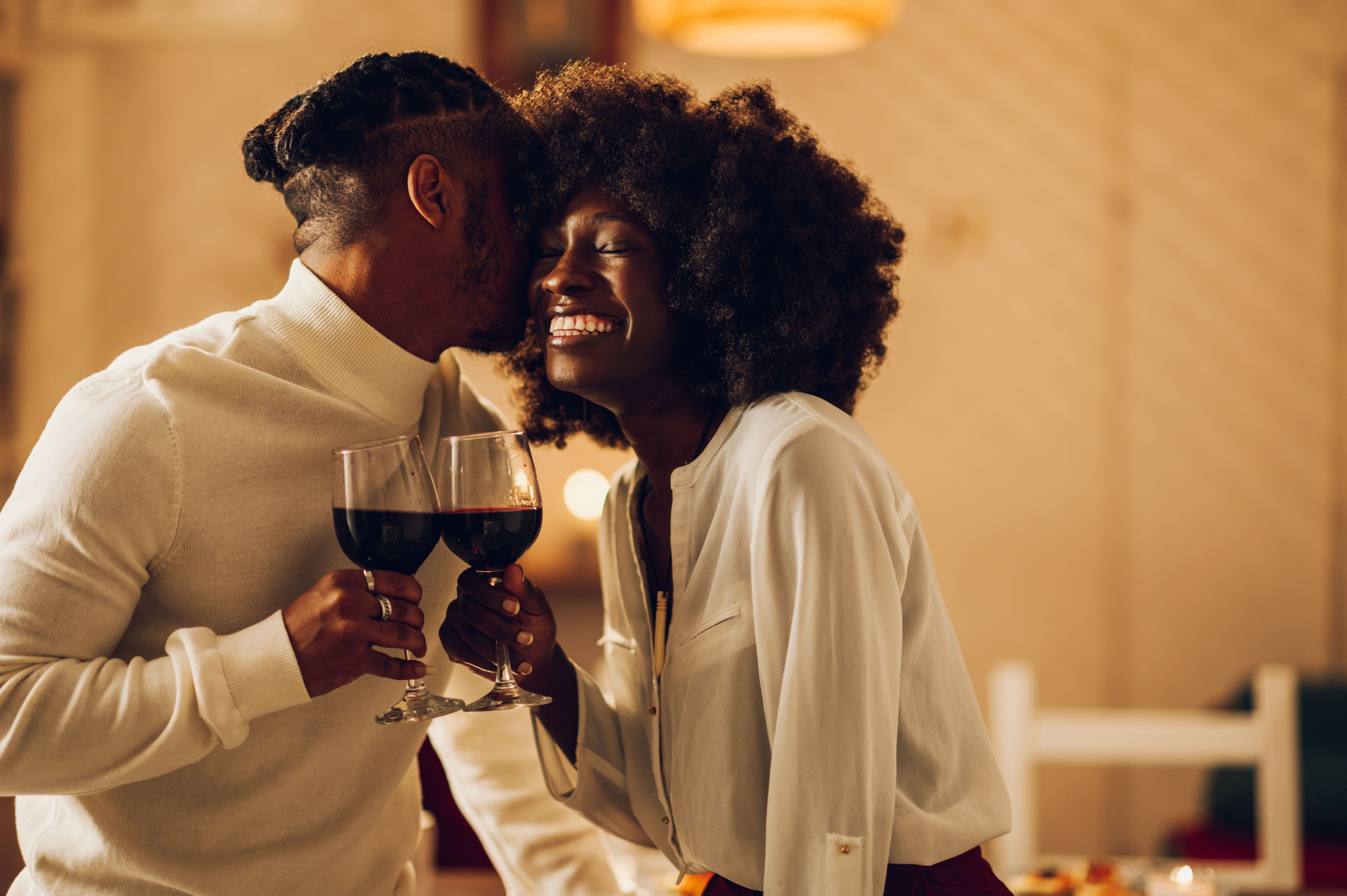 Beautiful passionate african american couple having a romantic candlelight dinner at home and celebrating their love together. Concept of love and relationship. Kissing and bonding. Copy space.