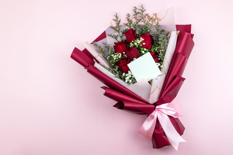 Red-roses-in-a-wrapped-bouquet-against-light-pink-background