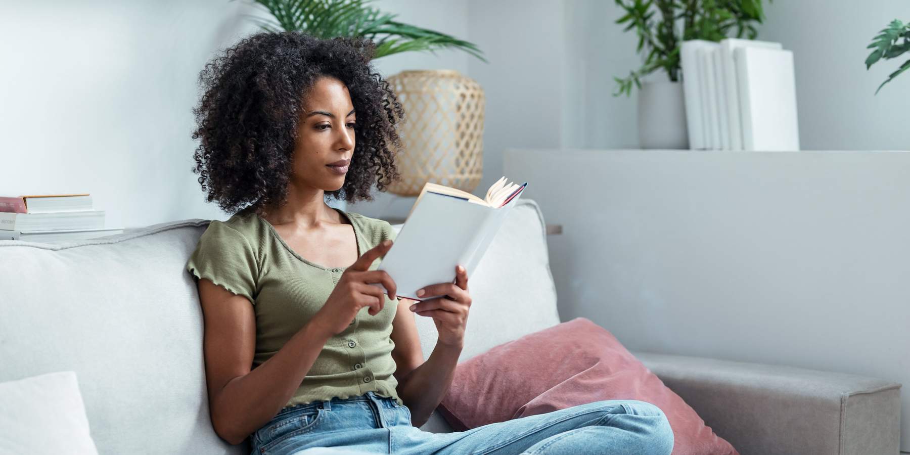 Shot of pretty young woman reading a book while sitting on sofa at home.