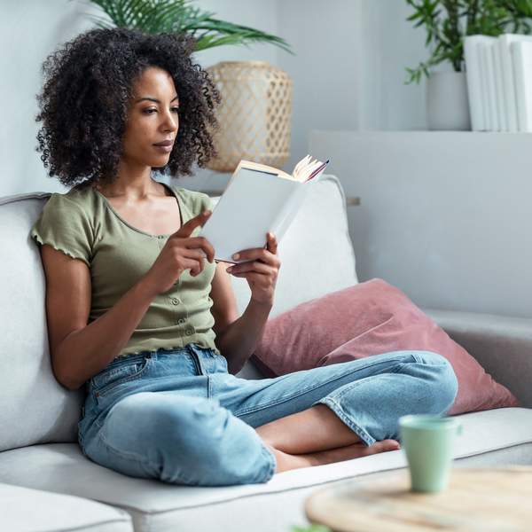 Shot of pretty young woman reading a book while sitting on sofa at home.
