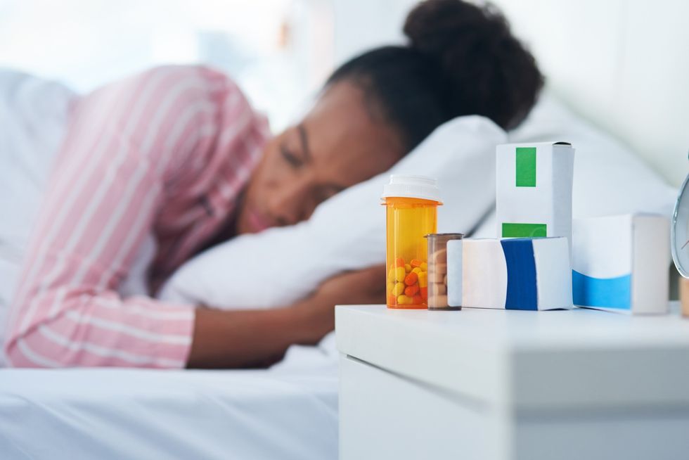 Sleeping-Black-woman-out-of-focus-behind-pill-containers-on-her-nightstand