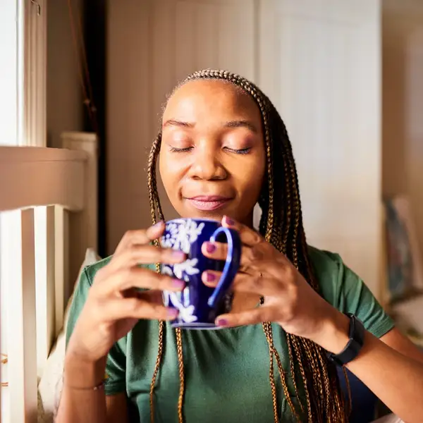 Smiling-Black-woman-with-closed-eyes-deep-breathing-as-she-sips-her-tea-in-bed