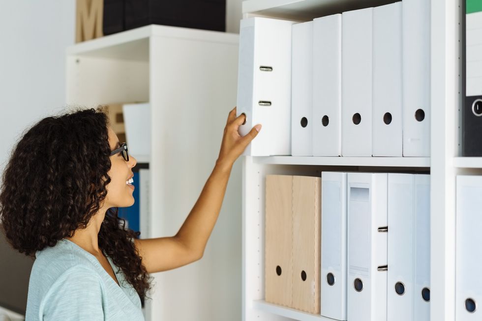 Smiling-woman-reaching-for-a-file-from-shelf-in-her-office-space