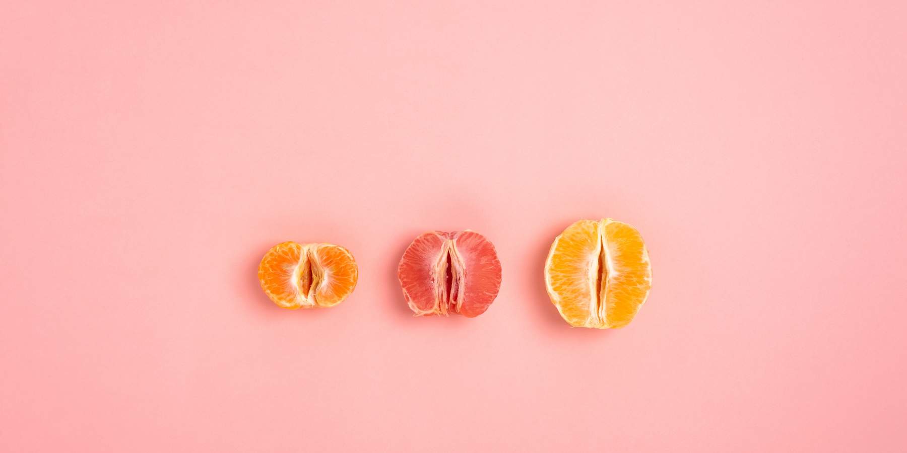 tangerine, grapefruit and orange cut in half on a peach background as a symbol of the vagina and female fertility, no people