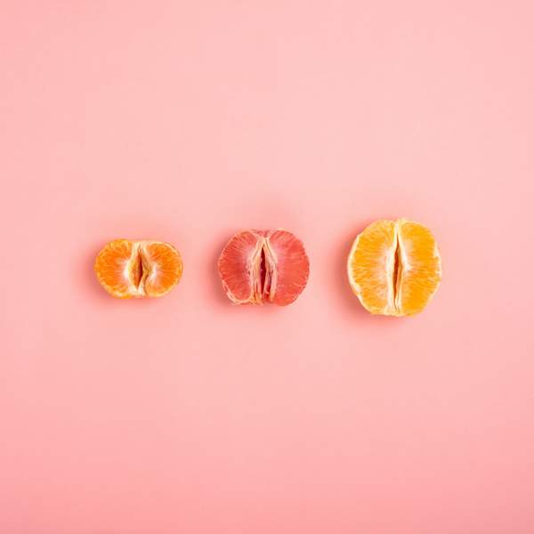tangerine, grapefruit and orange cut in half on a peach background as a symbol of the vagina and female fertility, no people