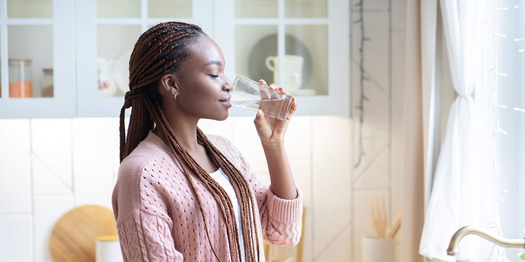 Thirsty African American Woman Drinking Water From Glass In Kitchen At Home, Young Black Female Standing Near Counter And Enjoying Heathy Refreshing Drink, Side View With Copy Space