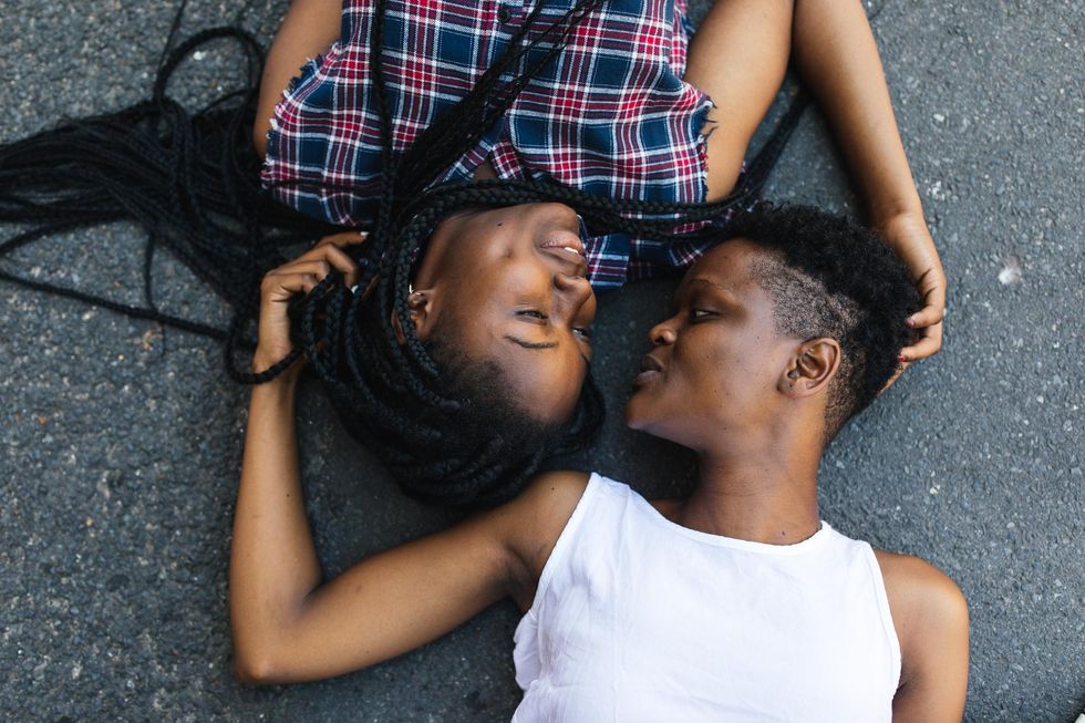two-black-women-talking-playfully-while-laying-down-against-tarmac