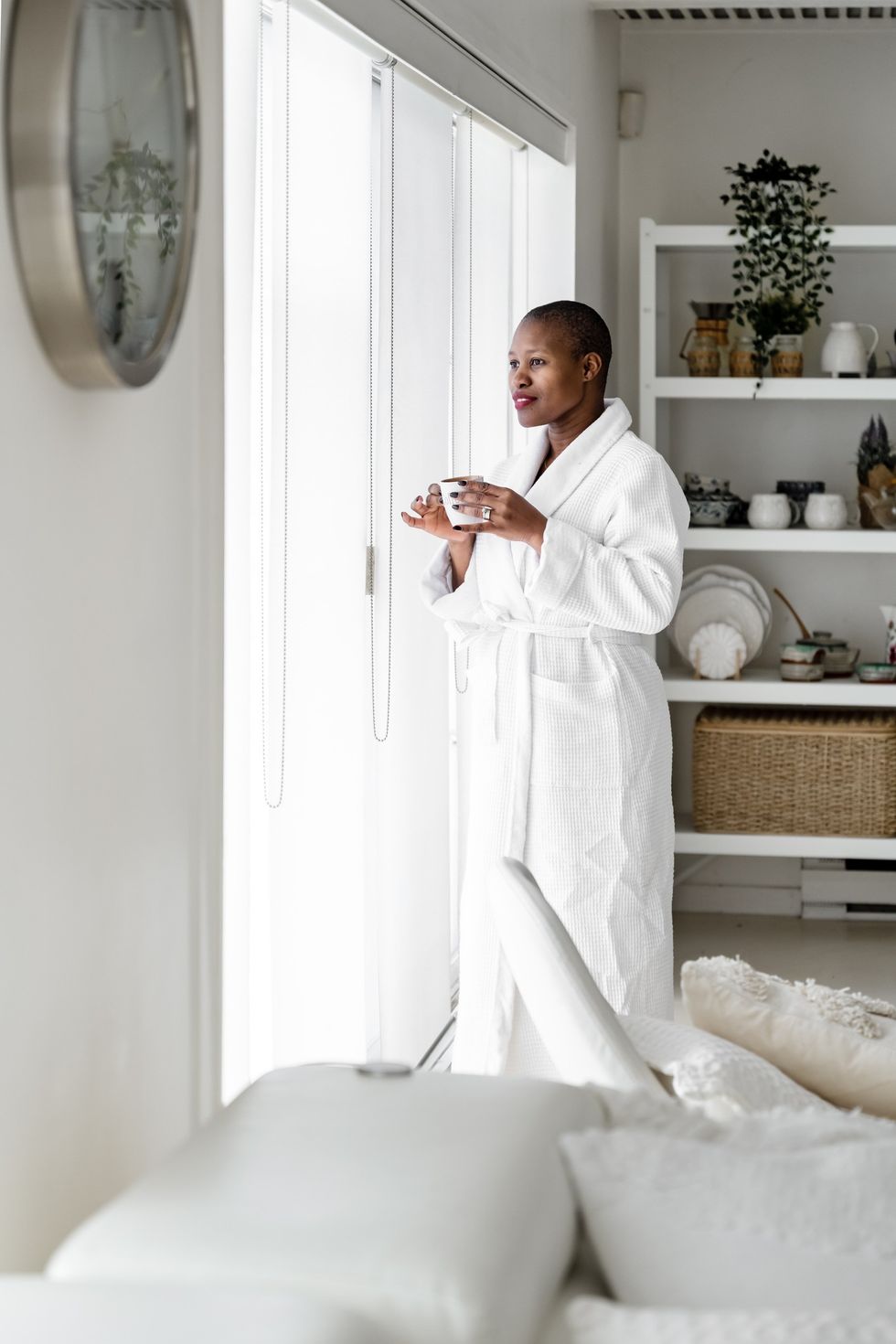 woman-enjoying-cup-of-coffee-staring-out-the-window-wearing-a-white-robe