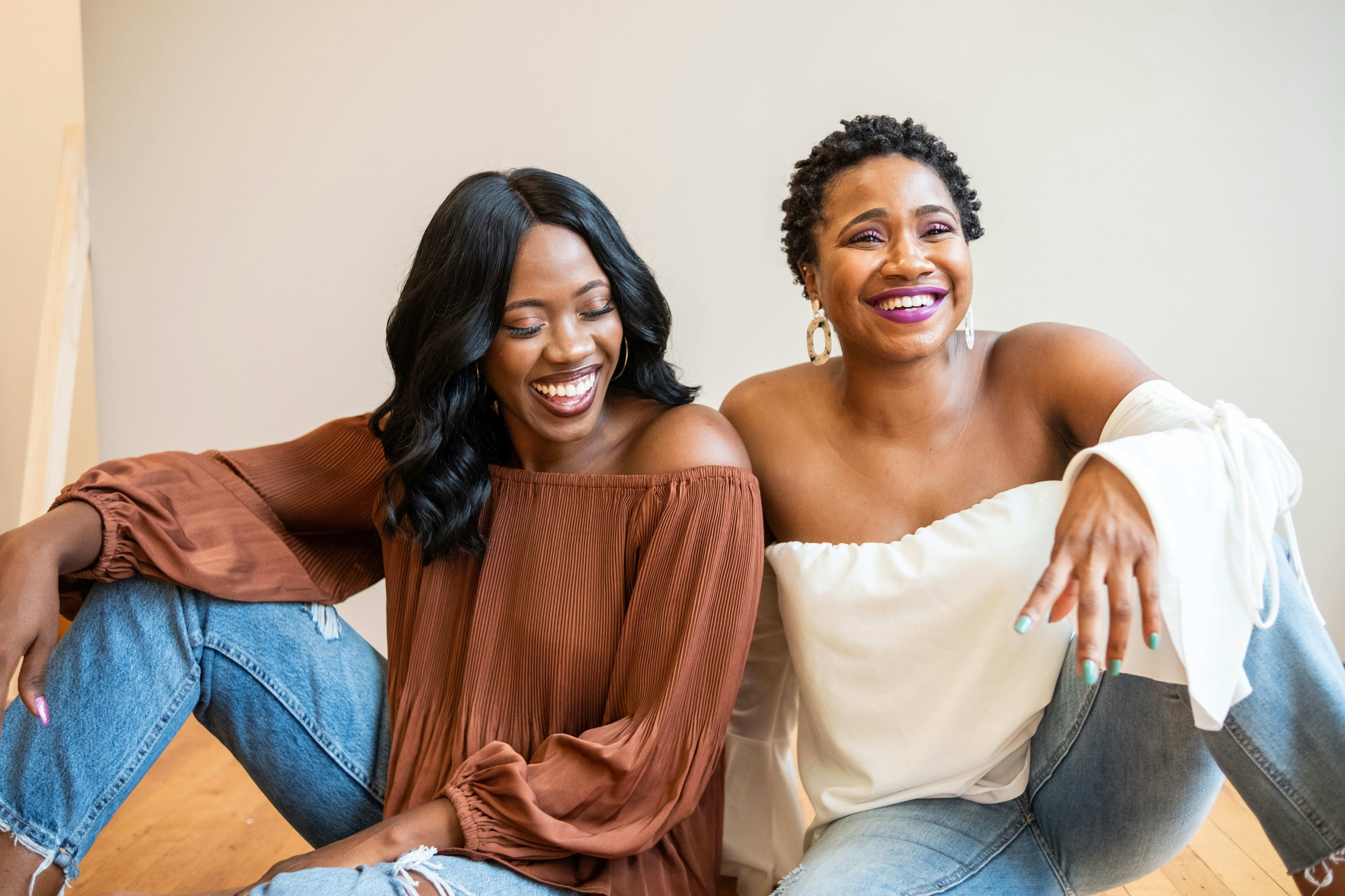 black-women-smiling-sitting-beside-one-another
