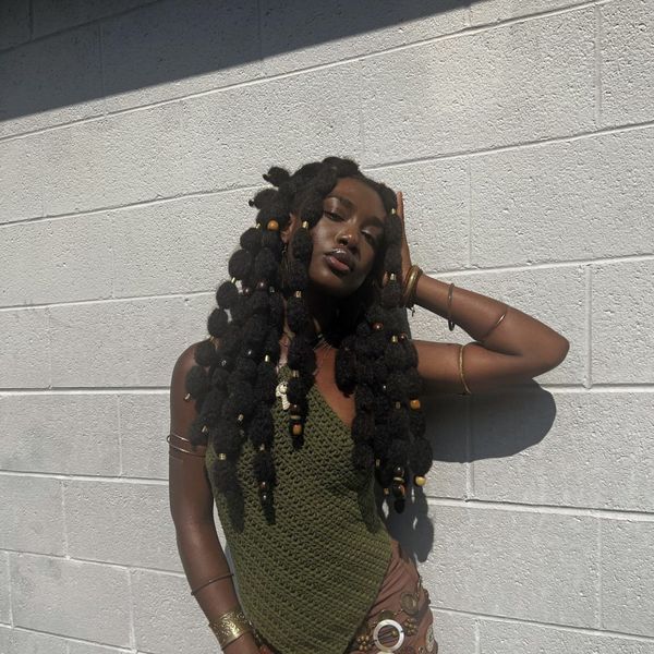 woman-wearing-bubble-braids-poodle-puffs-hairstyle-posing-against-white-brick-wall
